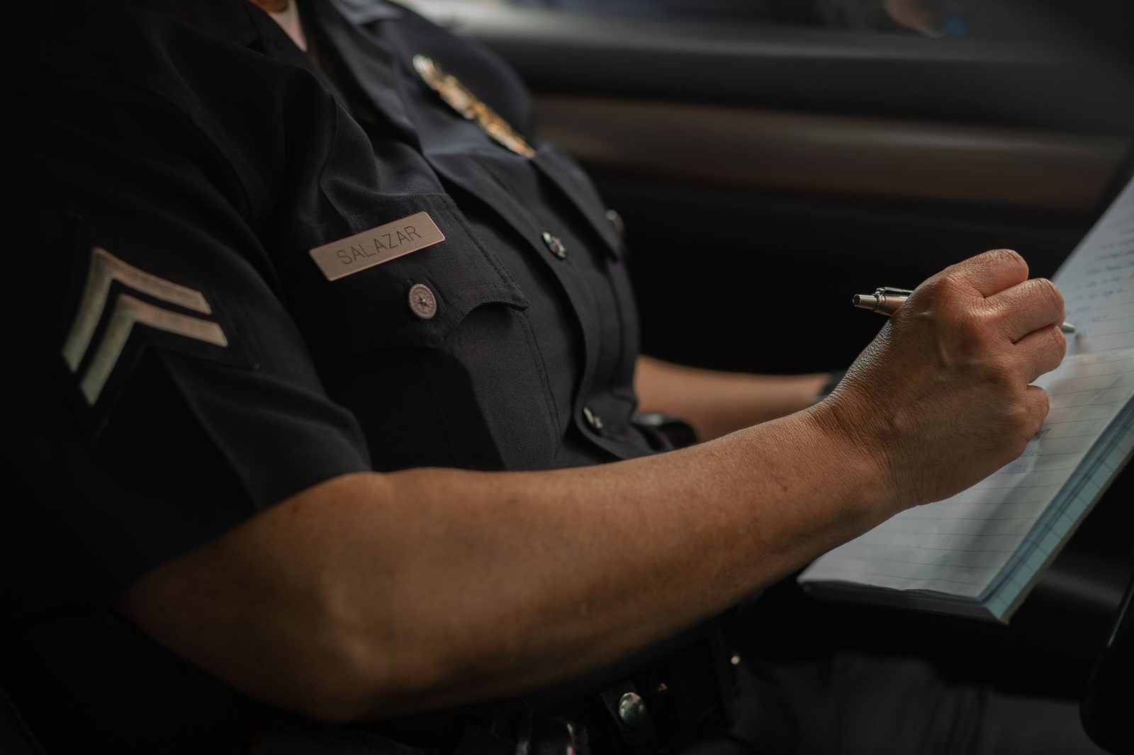 Police officer writing in notebook inside patrol car.