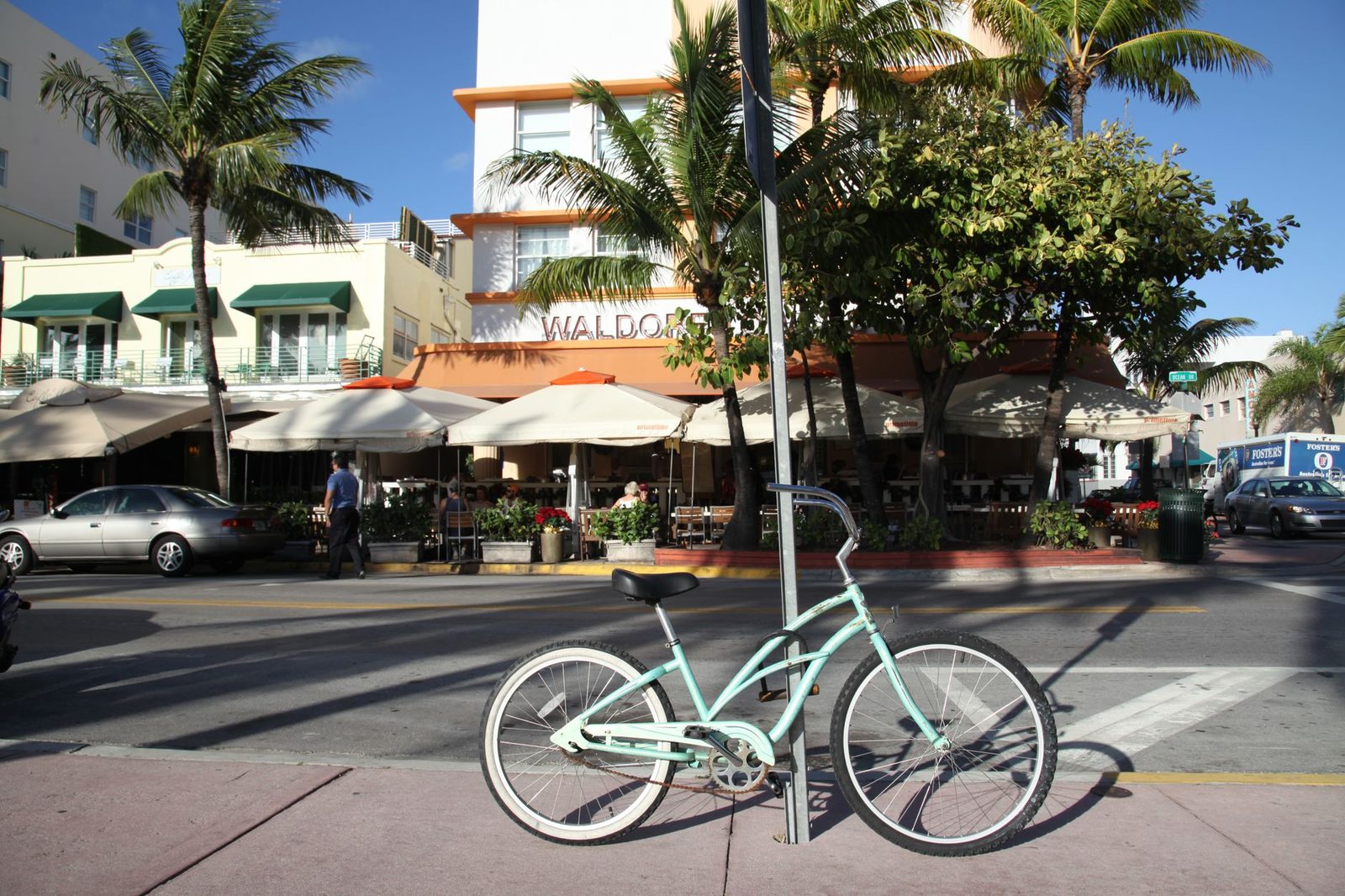 Una bicicleta estacionada en una calle soleada de Miami Beach, con palmeras y edificios art déco al fondo.