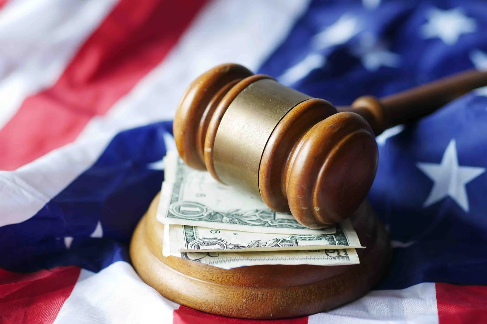 A gavel resting on dollar bills on top of the American flag.