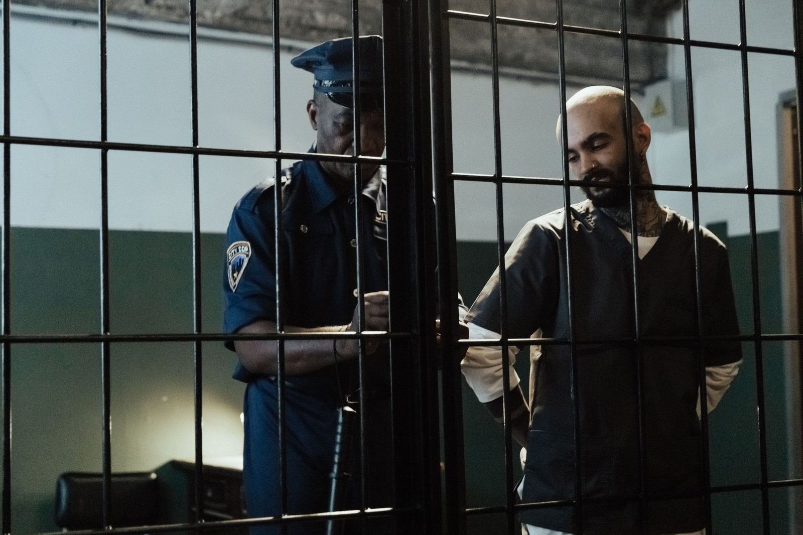 A police officer arrests a bald man in a dimly lit prison cell.