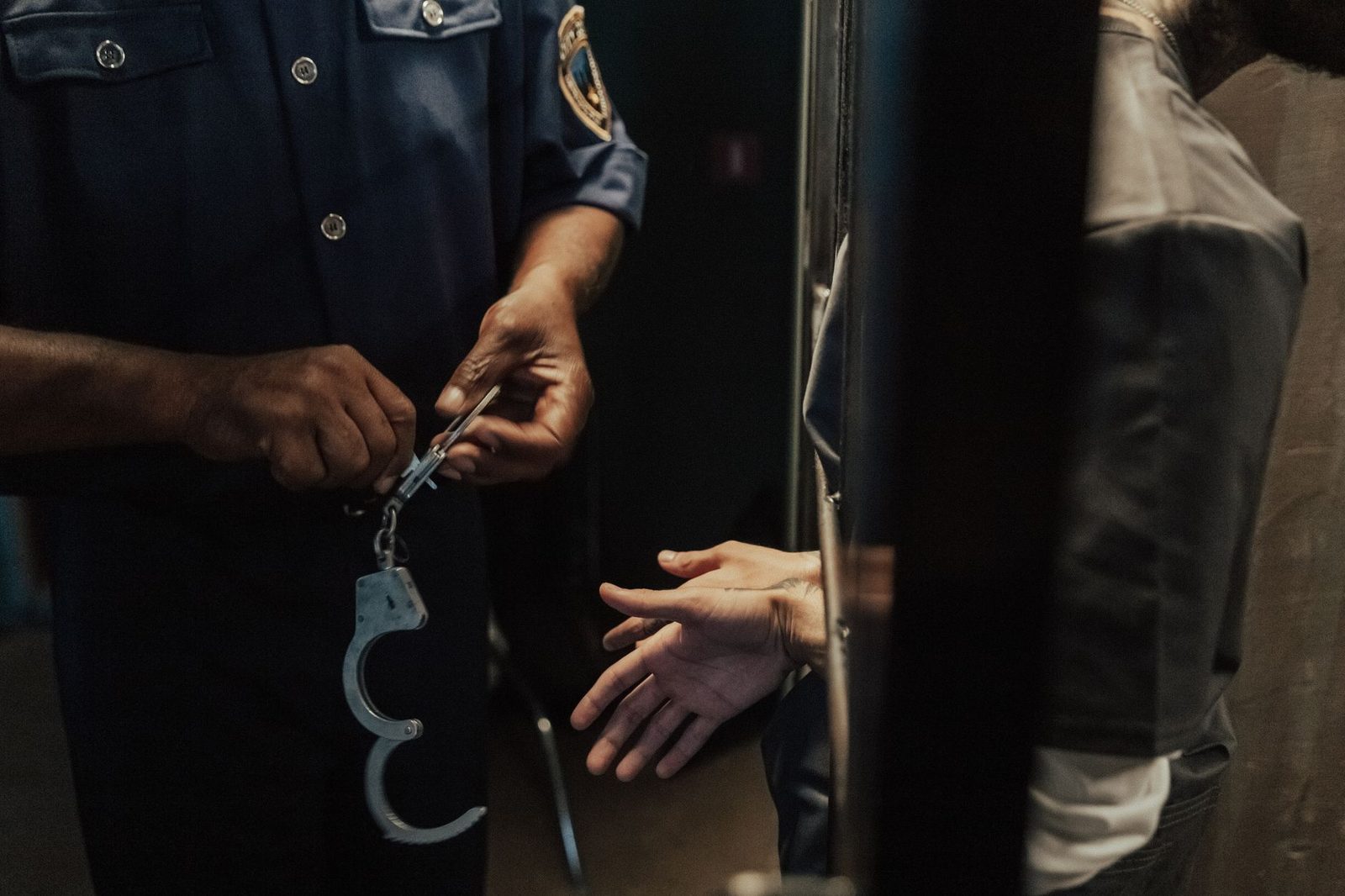 A police officer handcuffs a suspect indoors, with bars visible in the background.
