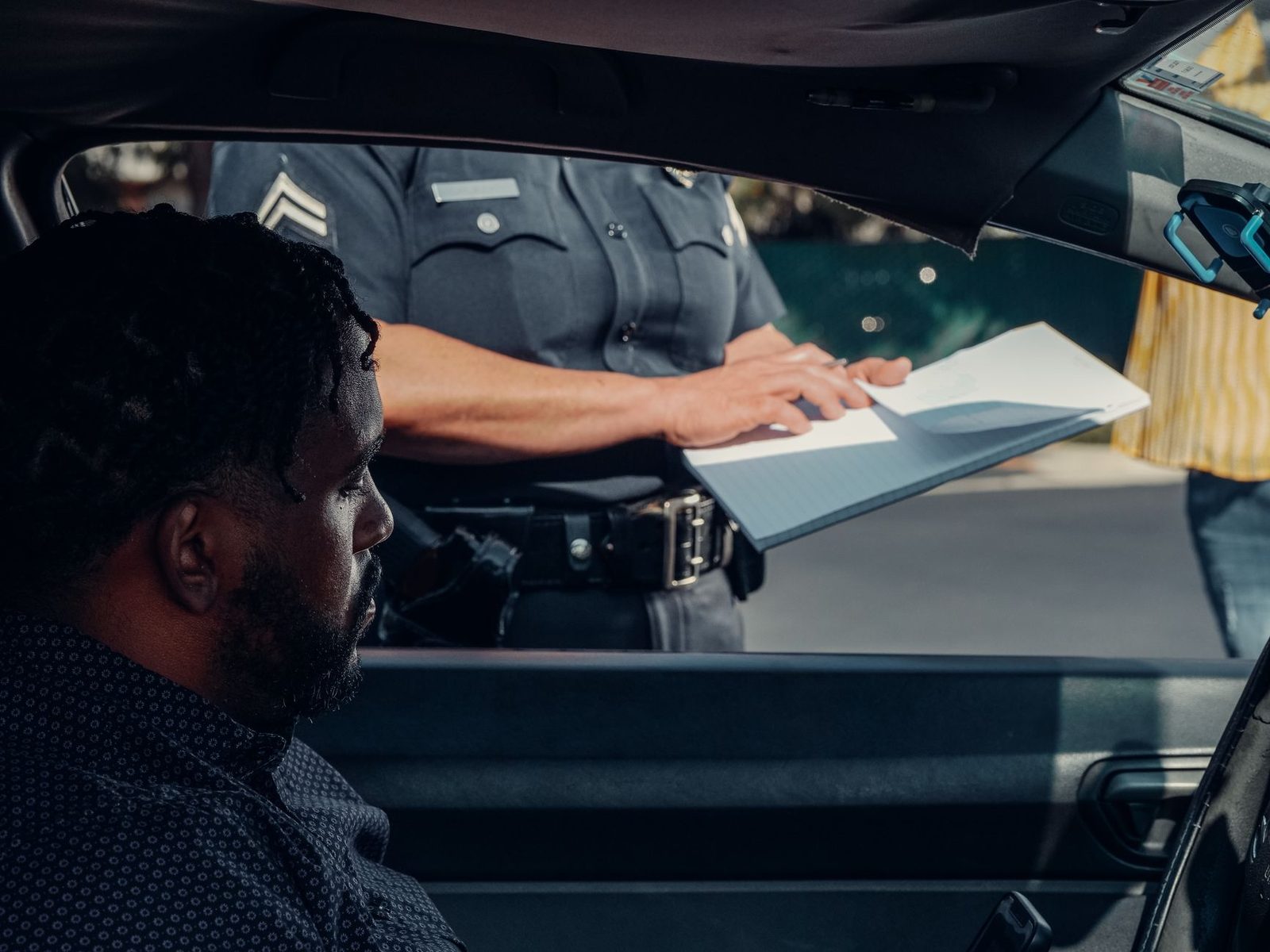 A police officer hands a traffic ticket to a driver through a car window.
