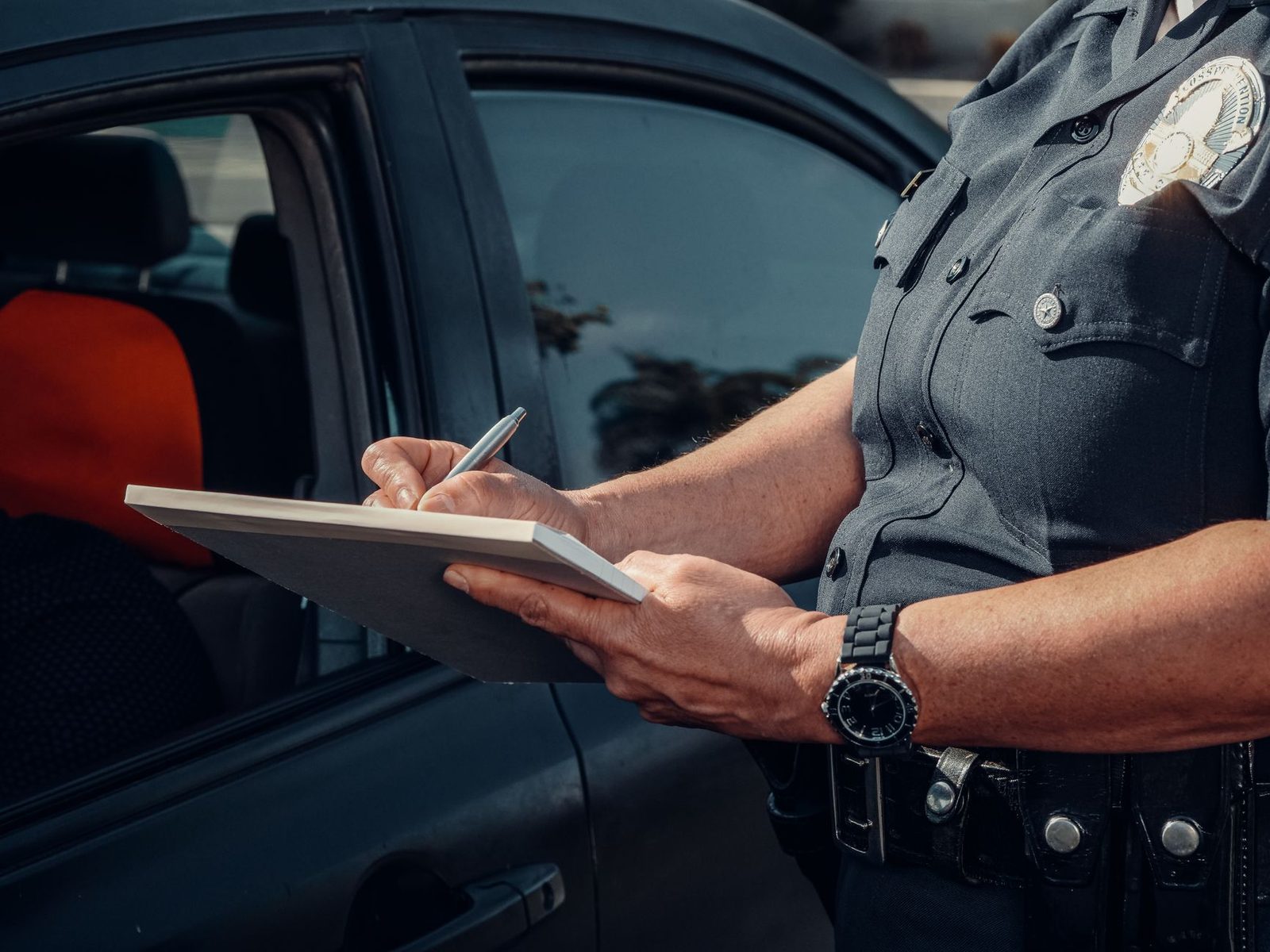 A close-up of a police officer writing a ticket beside a car window.