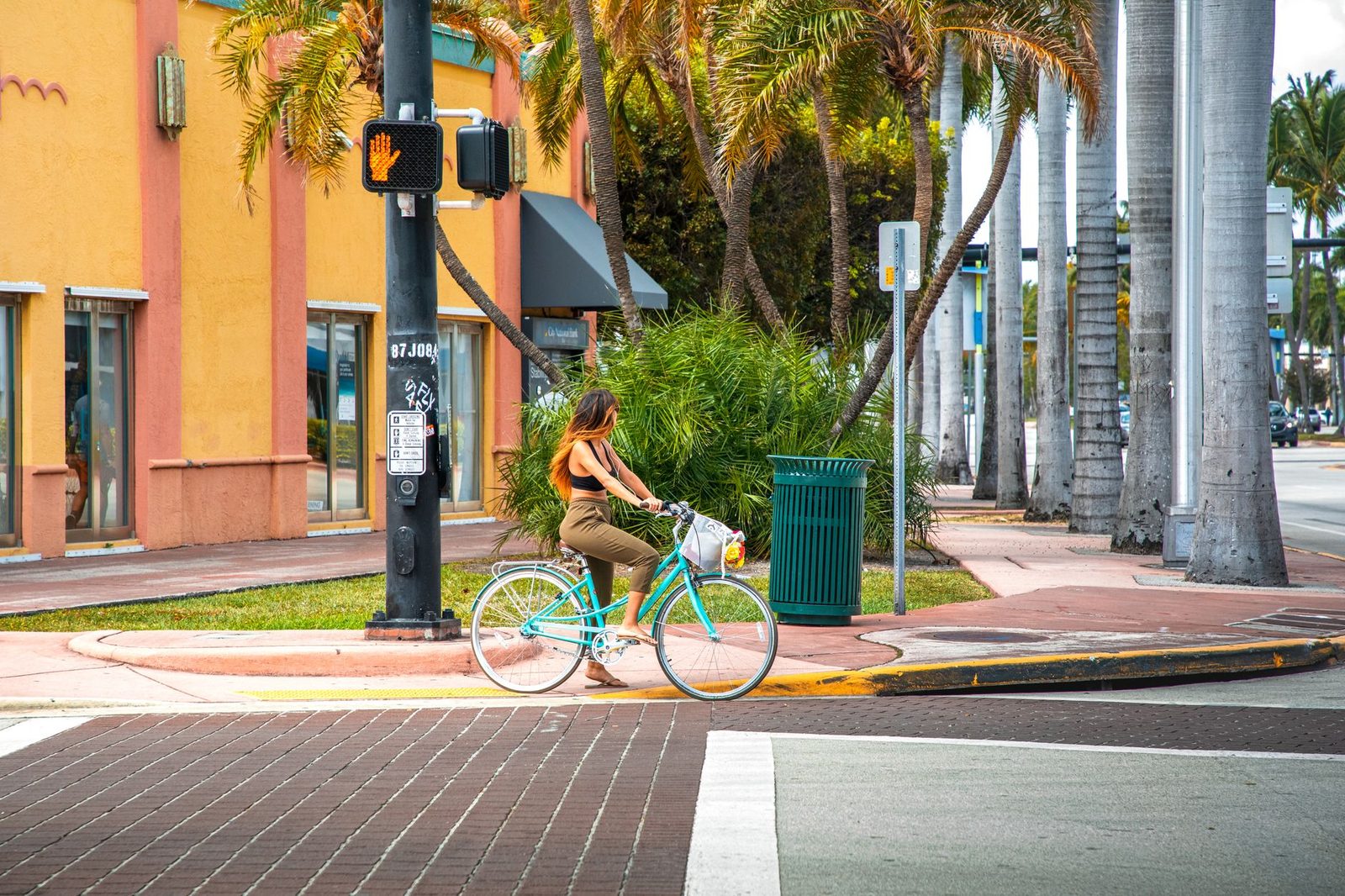Una mujer pasea en bicicleta junto a palmeras en una esquina colorida de Miami Beach.