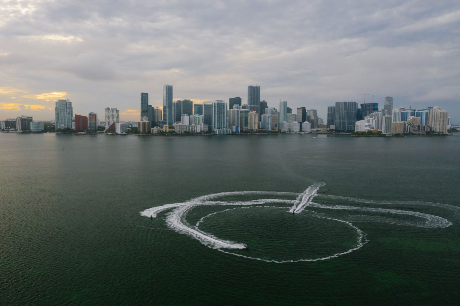 Aerial view of Miami's skyline with boat wakes trailing across the ocean surface.