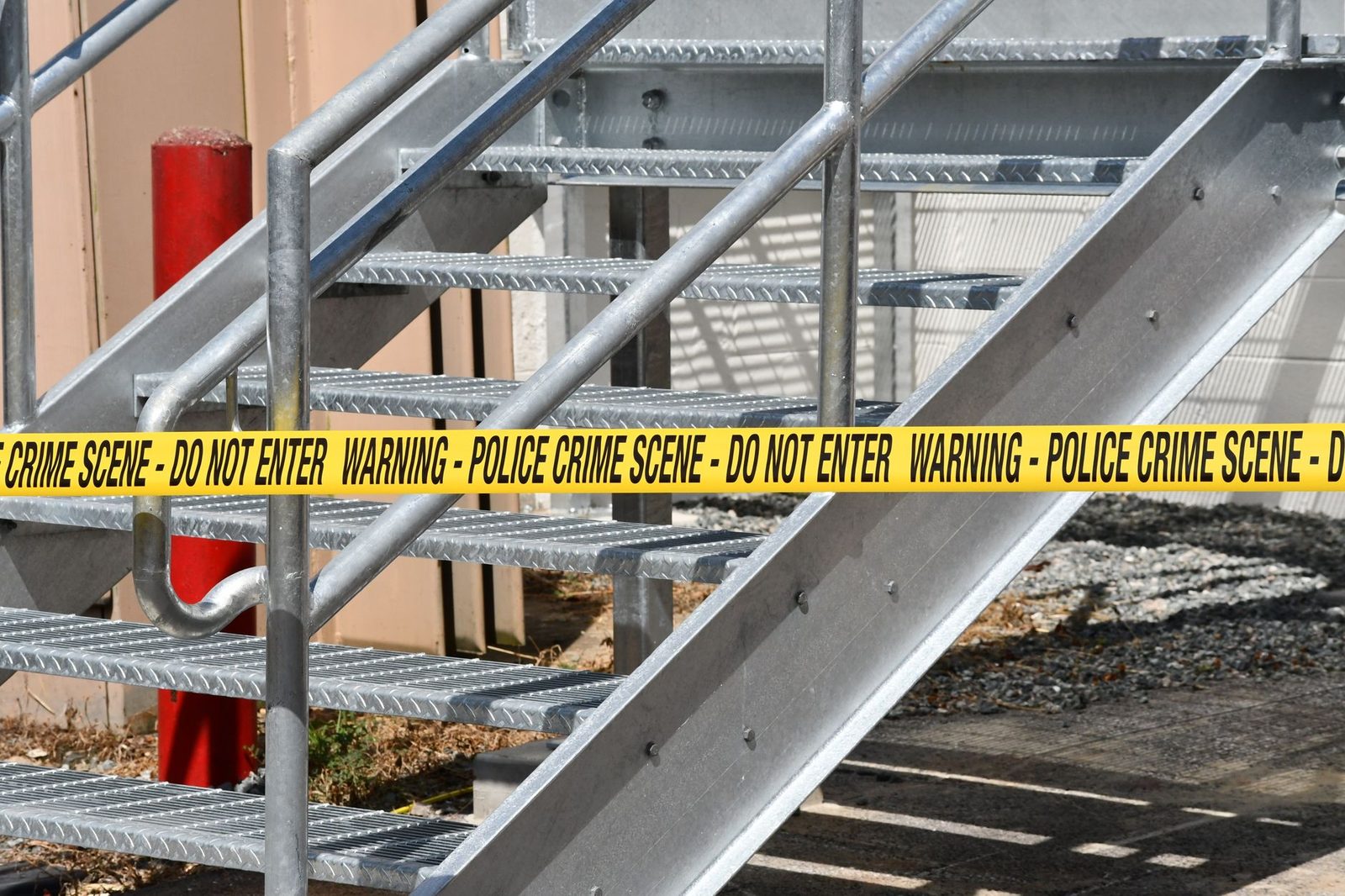 Close-up of yellow police crime scene tape blocking a metal stairway outdoors.