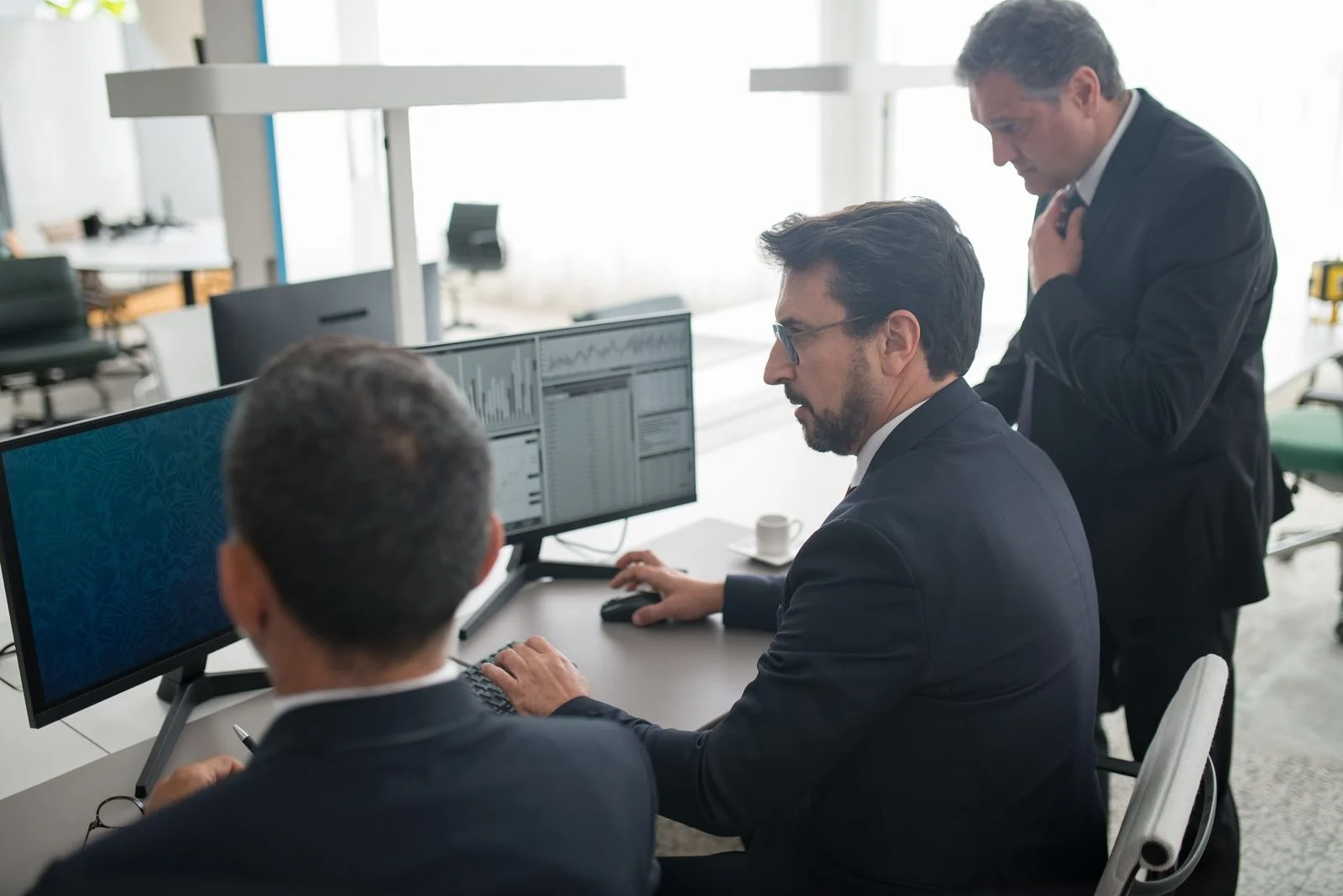 Colleagues in a modern office review stock market trends and data on multiple computer screens.