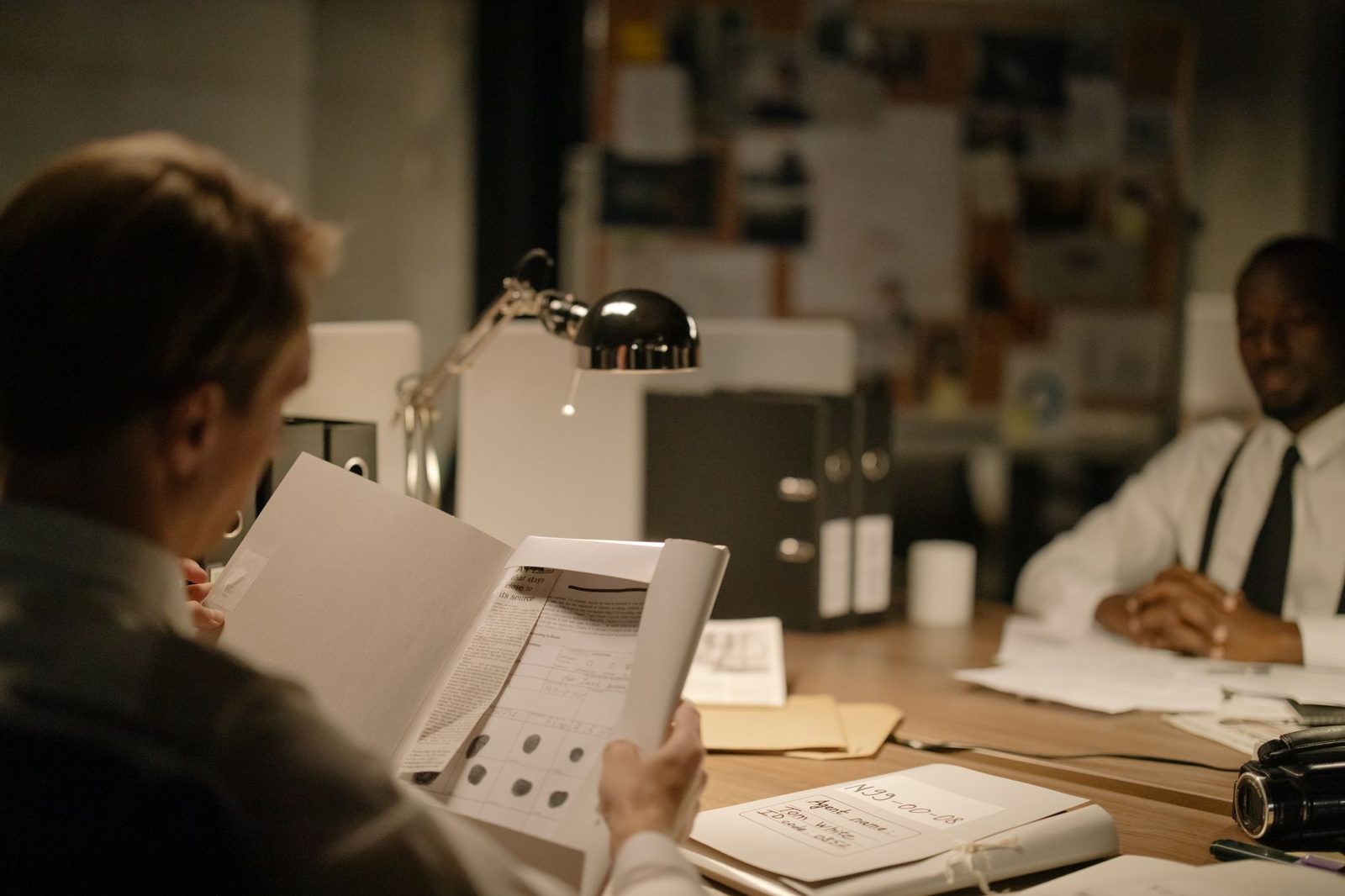 Detectives review documents together in a dimly lit office during a financial crime investigation.