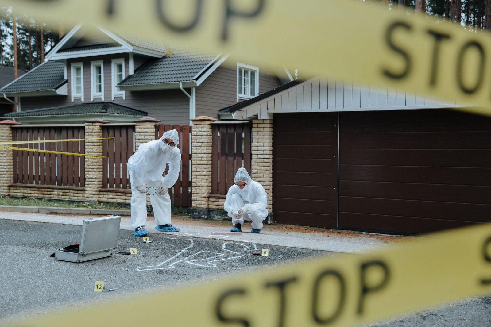 Forensic investigators work at an outdoor crime scene, marking evidence beside a chalk outline on the ground.