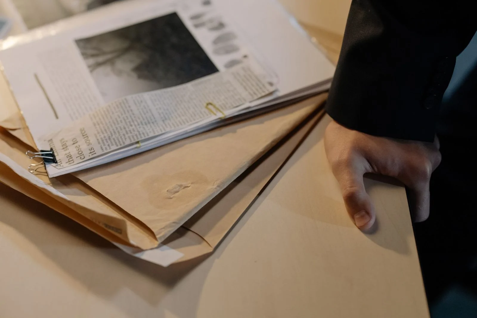 Una mano apoyada sobre un escritorio junto a una pila de documentos y recortes de periódico.