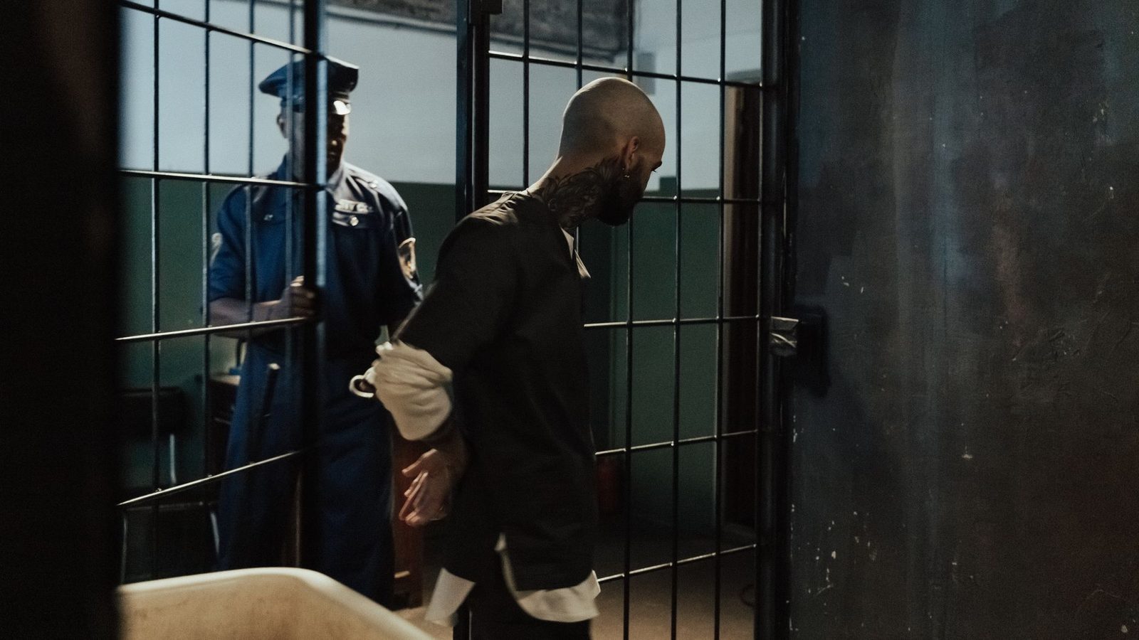 Handcuffed person being escorted through a jail corridor by a police officer.