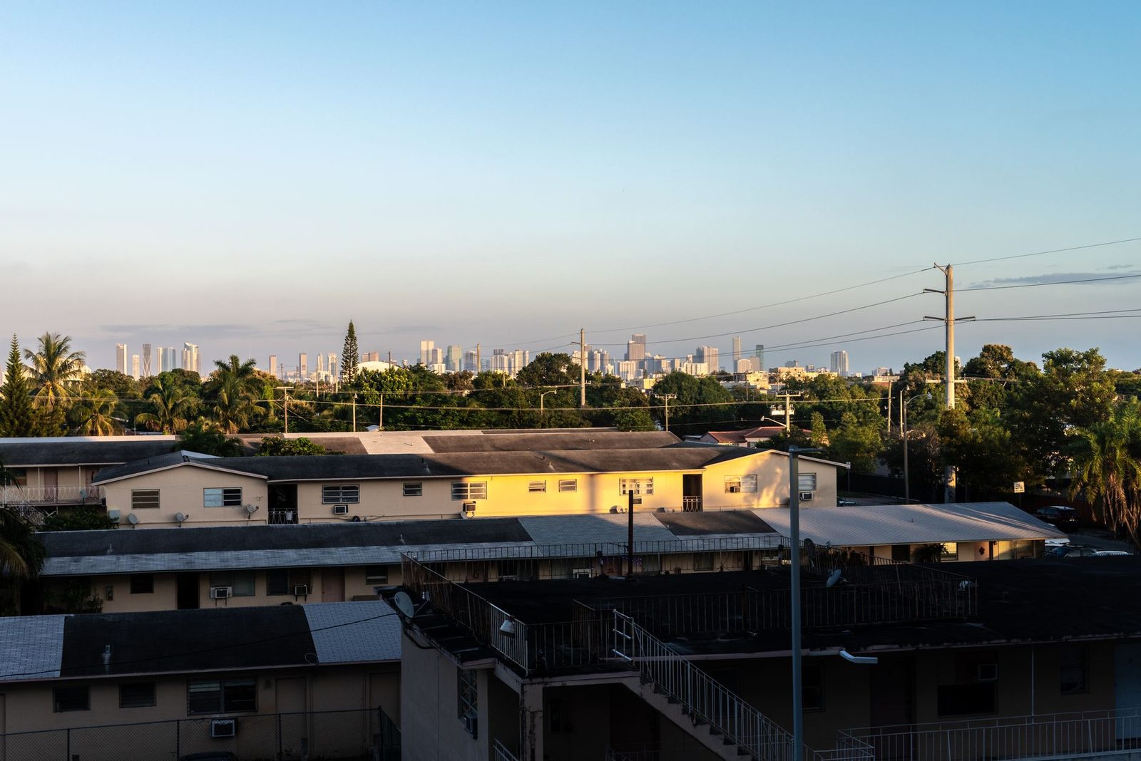 Miami skyline at sunset, viewed from Coral Gables over residential rooftops in the foreground.