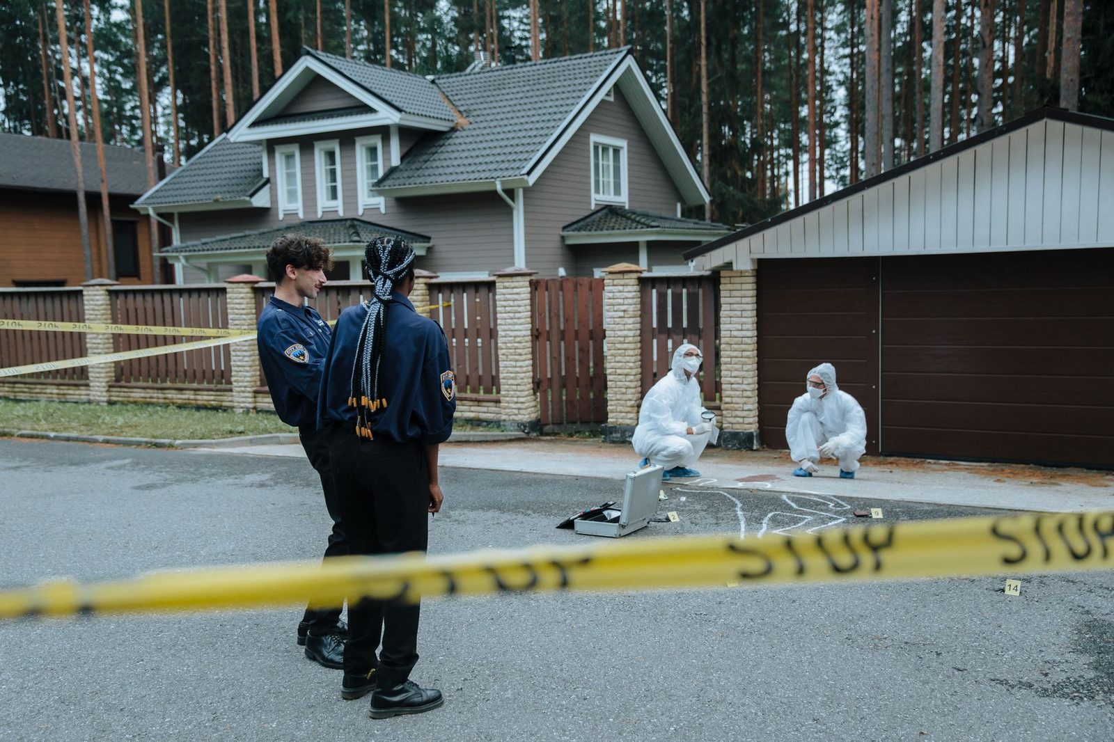 Agentes de policía y peritos forenses examinan una escena frente a casas en una zona residencial.