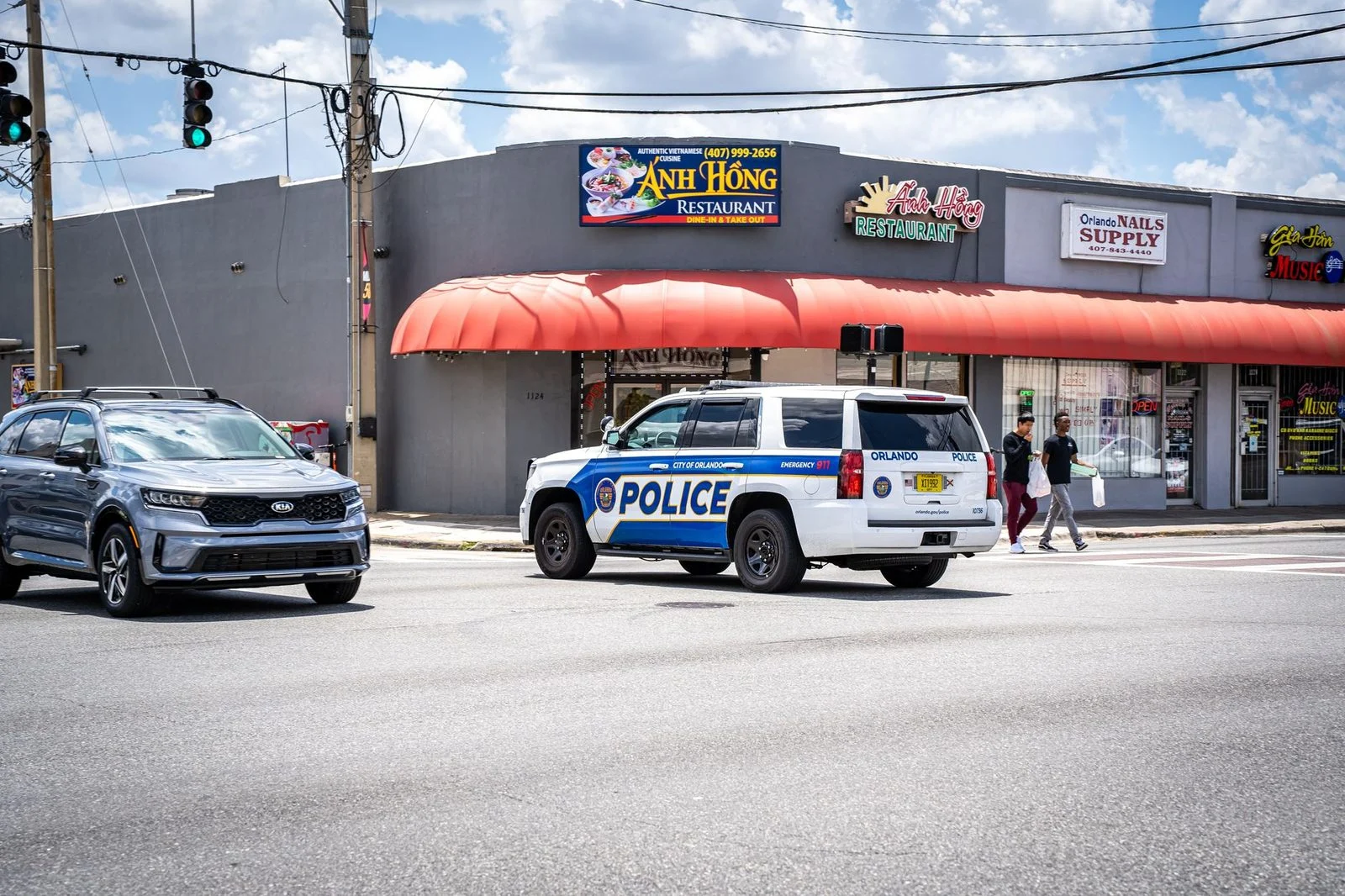 Police vehicle driving down an Orlando street with traffic and pedestrians under a sunny sky.