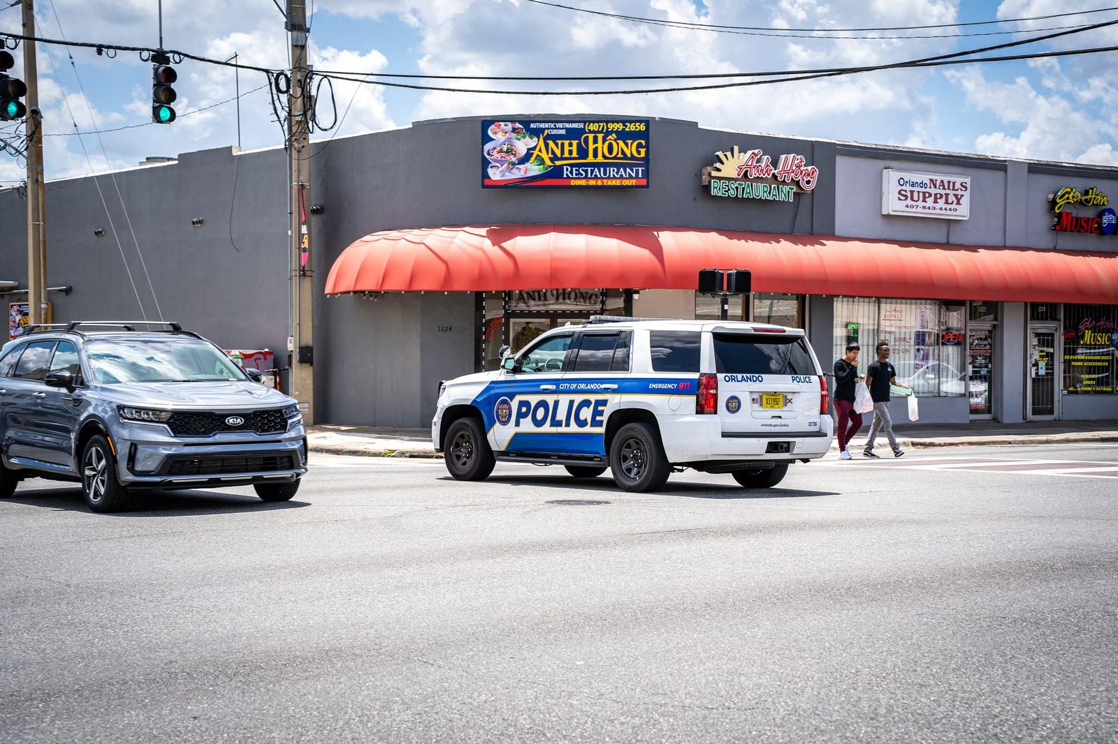 Police car driving on a sunny Orlando street with traffic and pedestrians nearby.