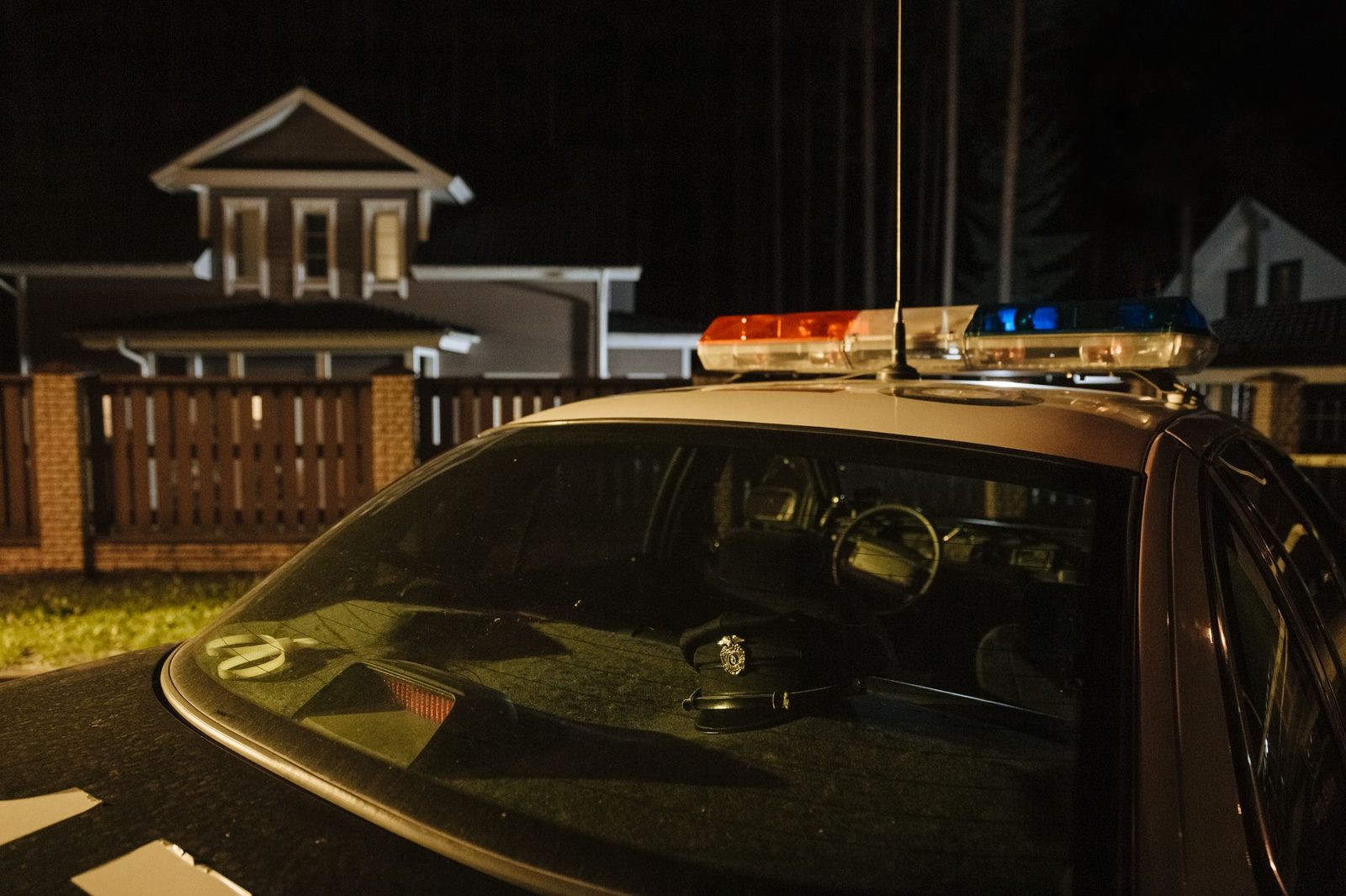 Police car parked on suburban street at night with house lights visible.
