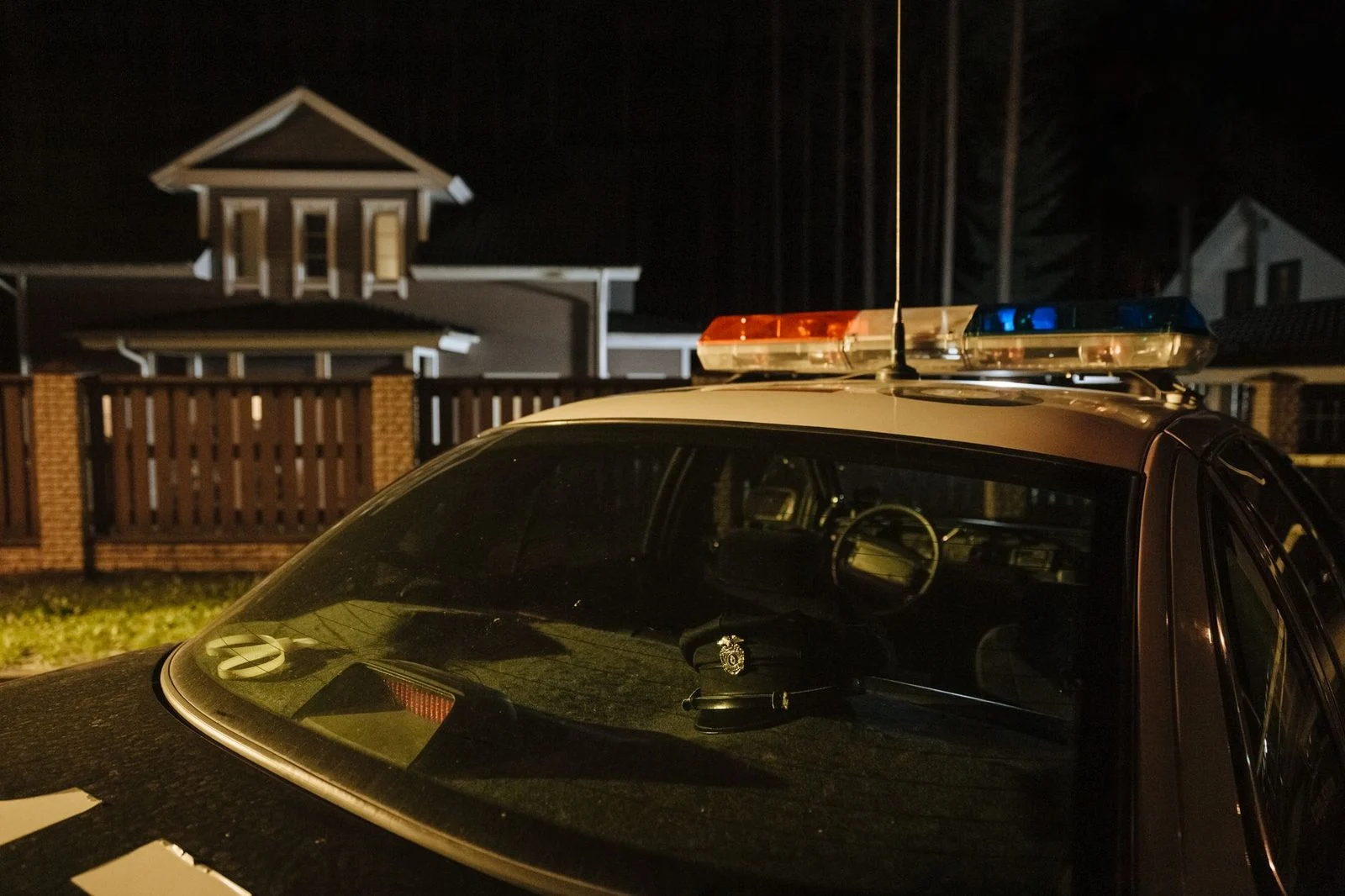 A parked police car at night in front of suburban houses with their lights on.
