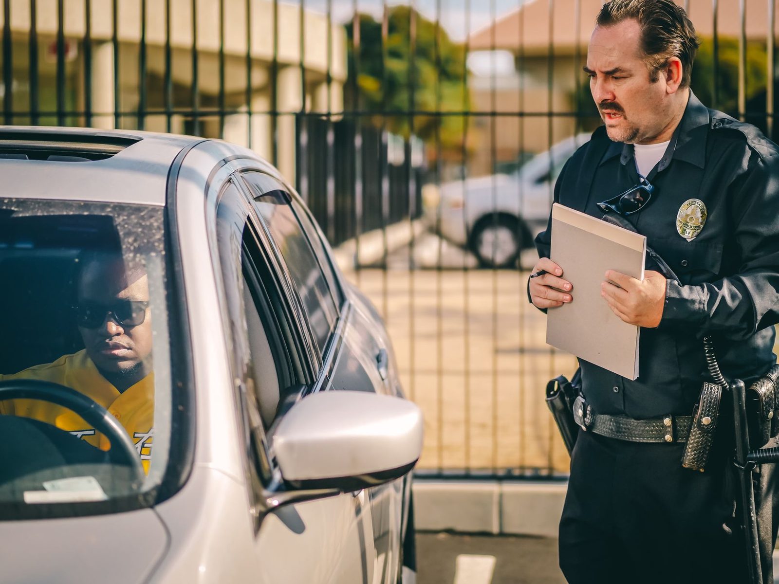 Police officer at a car window handing a ticket to a driver on a sunny day.