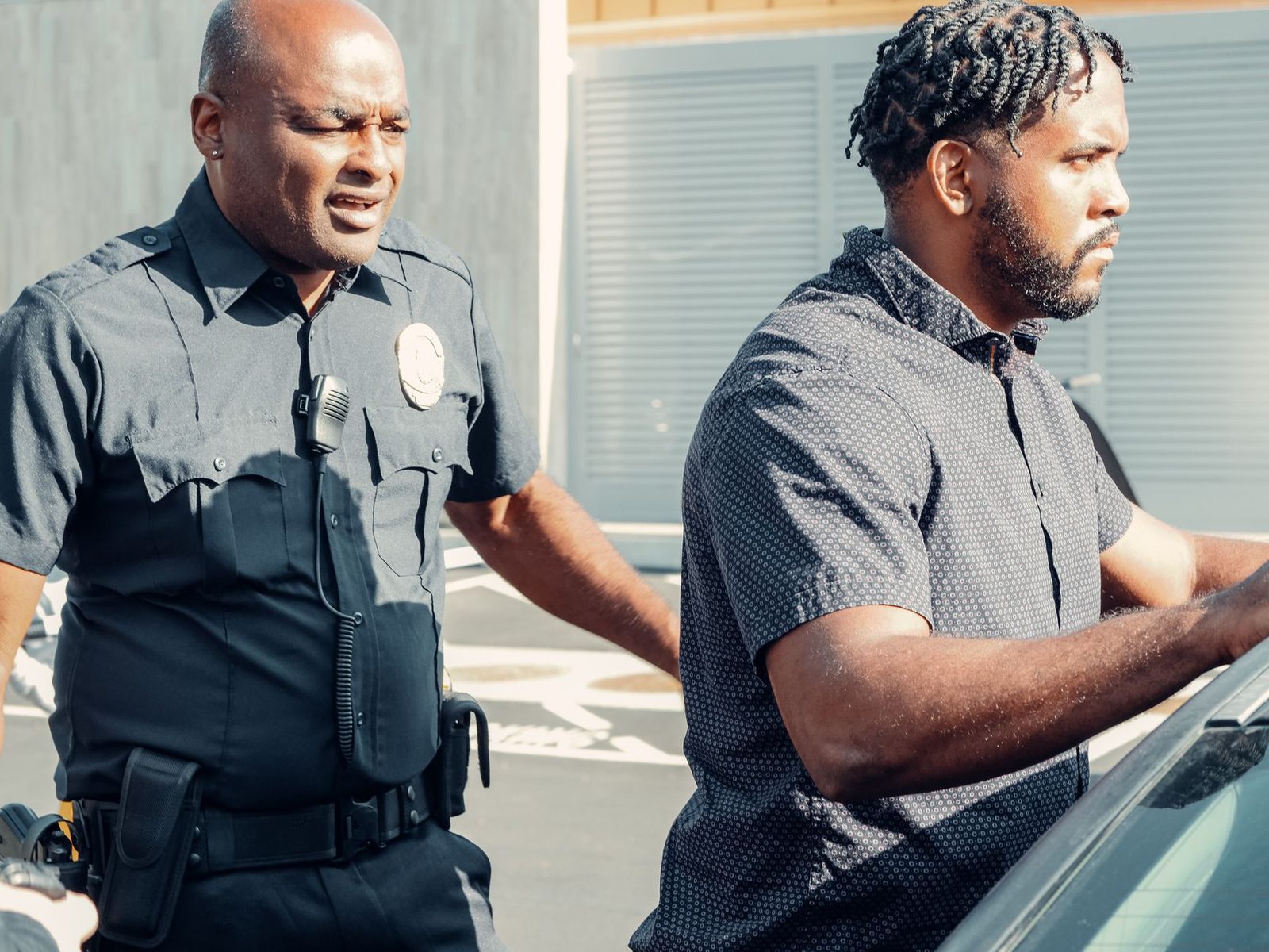 Police officer detaining a man beside a car during a traffic stop.