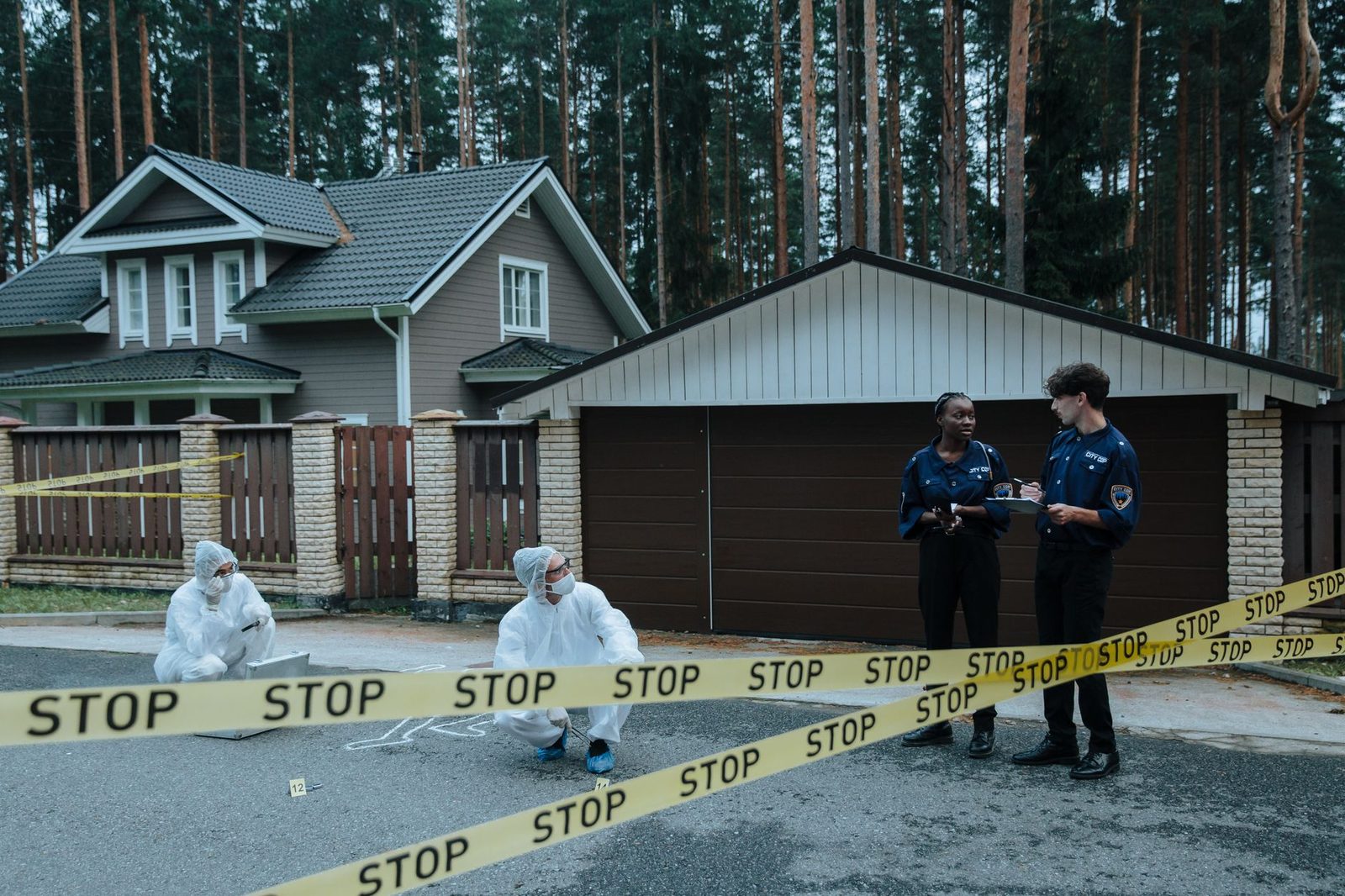Agentes de policía e investigadores forenses trabajan en una escena del crimen frente a una casa suburbana.