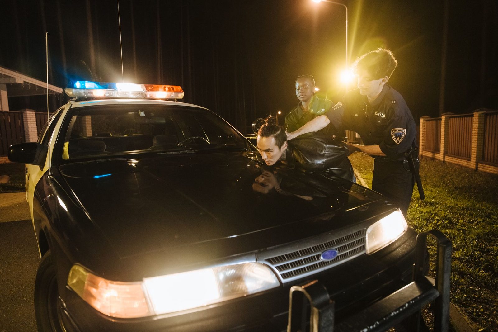 Police officers apprehending a suspect at night near a patrol car.