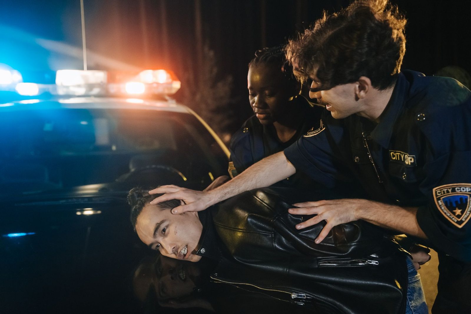 Police officers arresting a suspect at night with flashing lights visible.