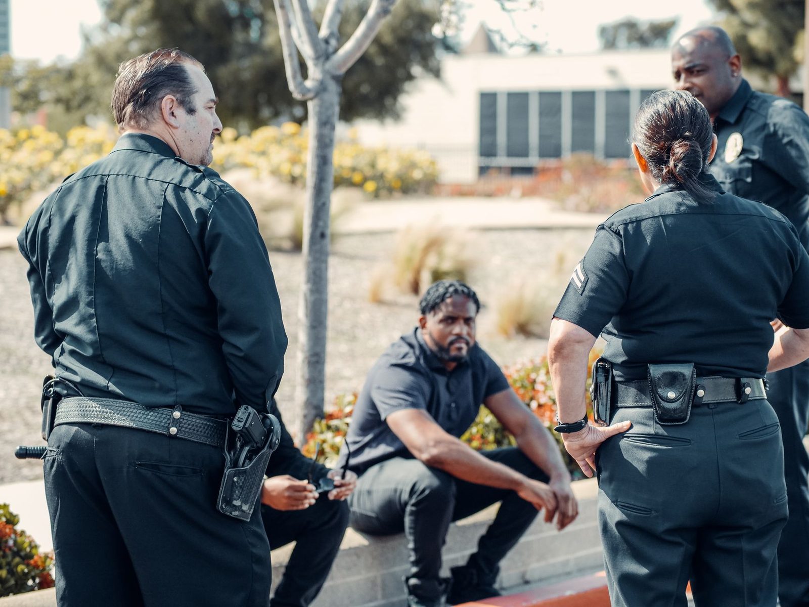 Police officers speaking with a seated person outdoors.