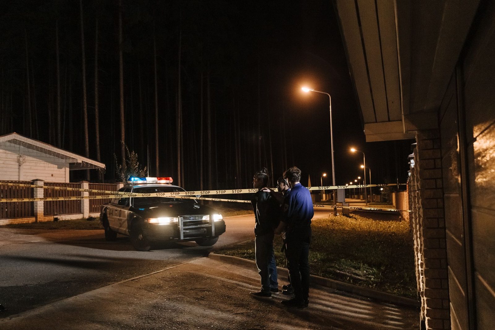 Agentes de policía trabajan en una escena nocturna junto a una patrulla, con cinta de precaución bajo las farolas.