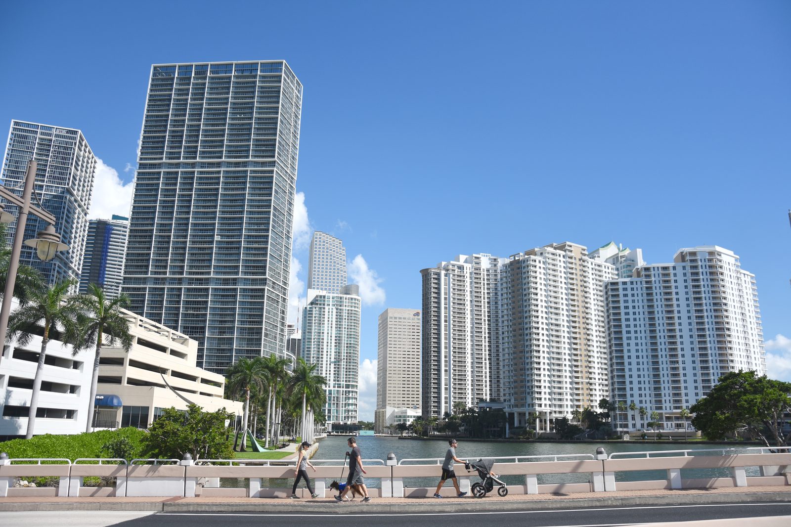 Downtown Miami skyscrapers under a clear blue sky, with pedestrians crossing a bridge.