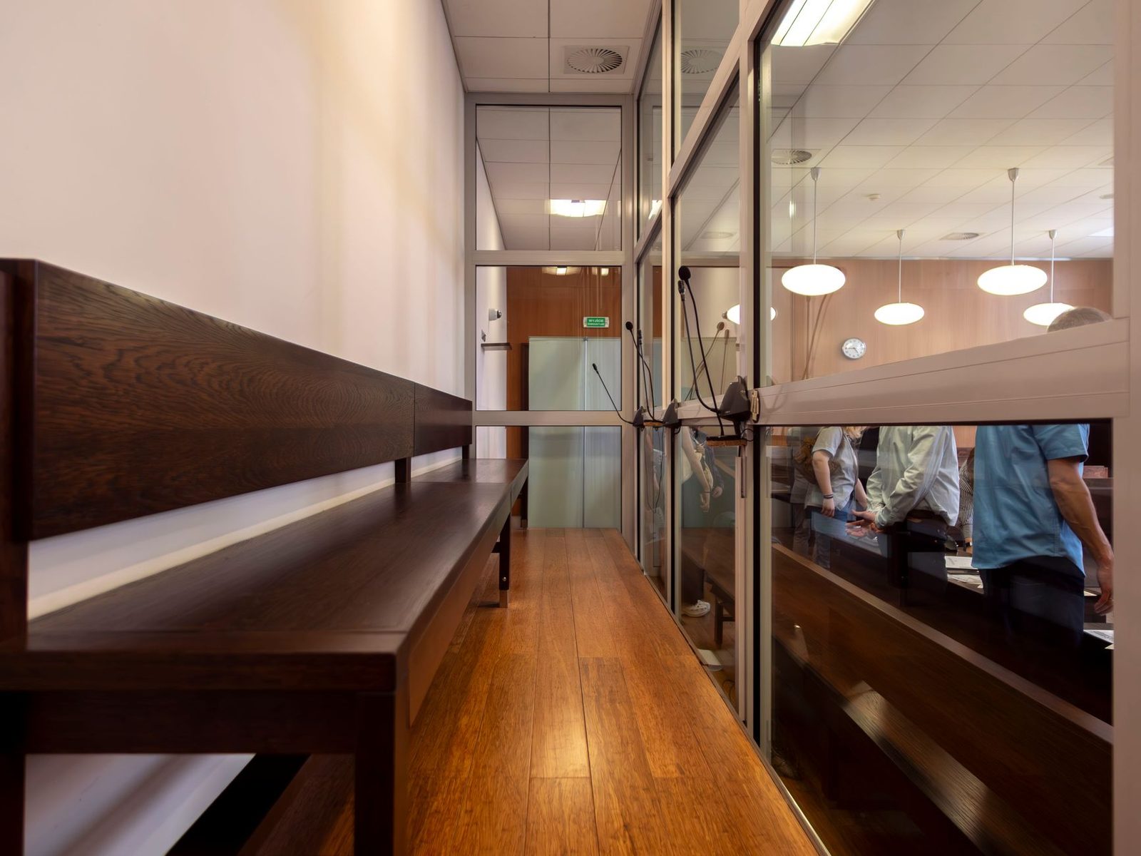 Sala de tribunal con bancos de madera y divisiones de vidrio.