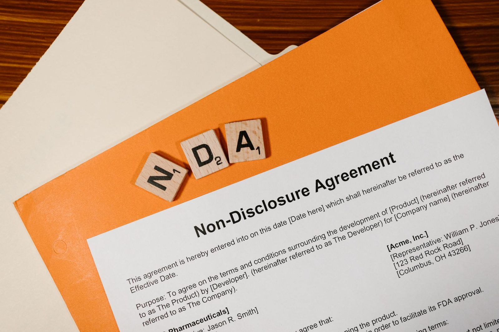 Scrabble tiles spelling "NDA" sit on a printed non-disclosure agreement, suggesting confidentiality.