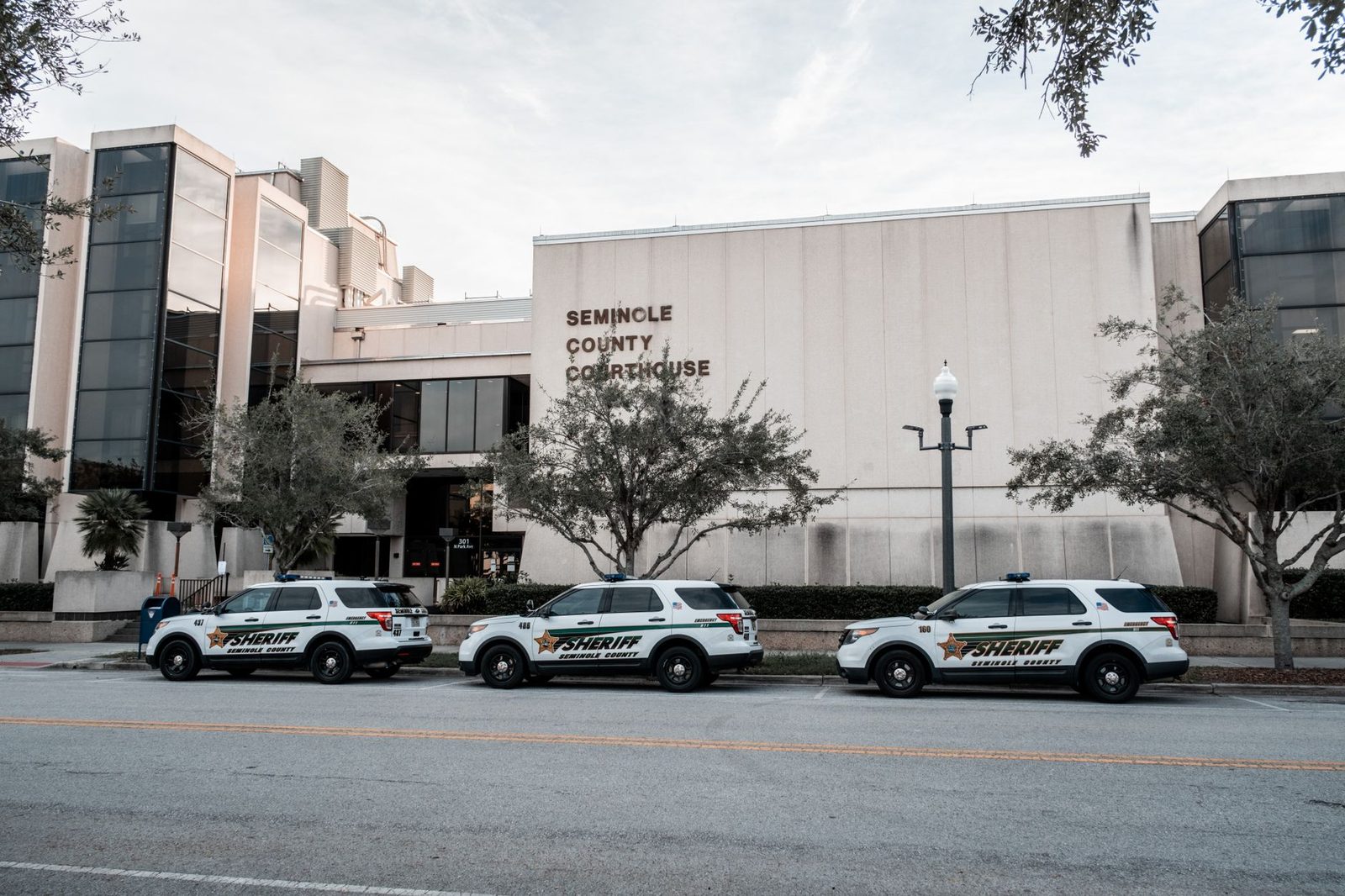 Vehículos del sheriff estacionados frente al edificio del tribunal del condado de Seminole, de día.