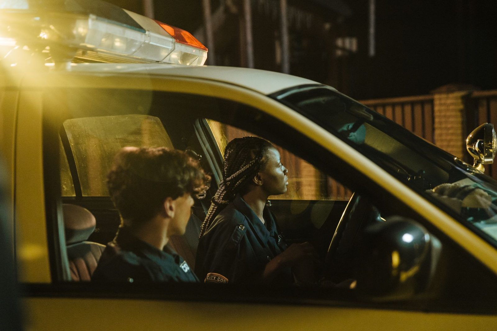 Two police officers sit in a patrol car at night, watching their surroundings.