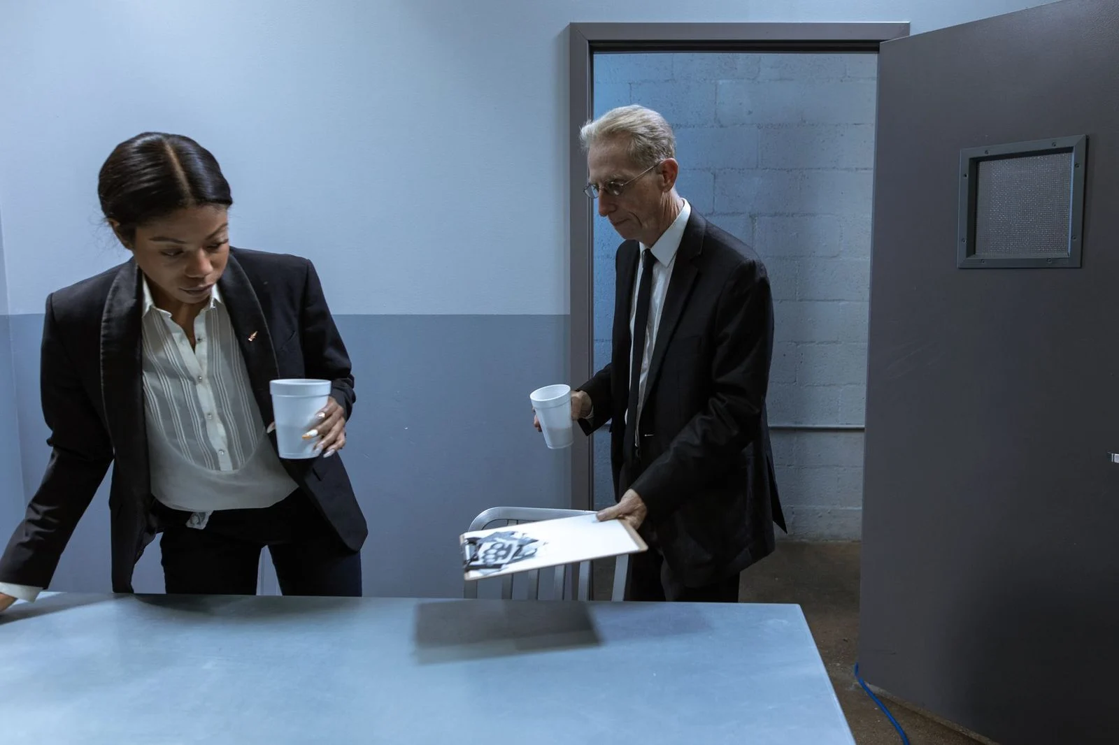 Two professionals sit across a desk in a secure office, reviewing confidential documents over coffee.