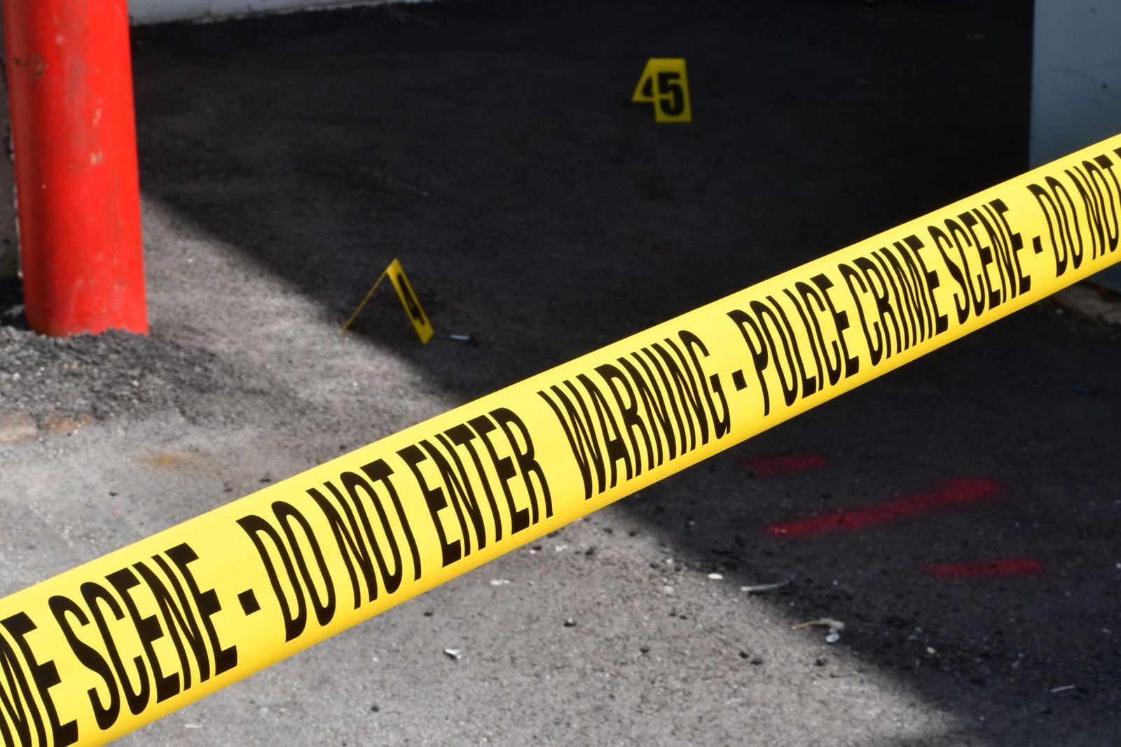 Yellow police crime scene tape stretches across a concrete street, marking off a restricted area.
